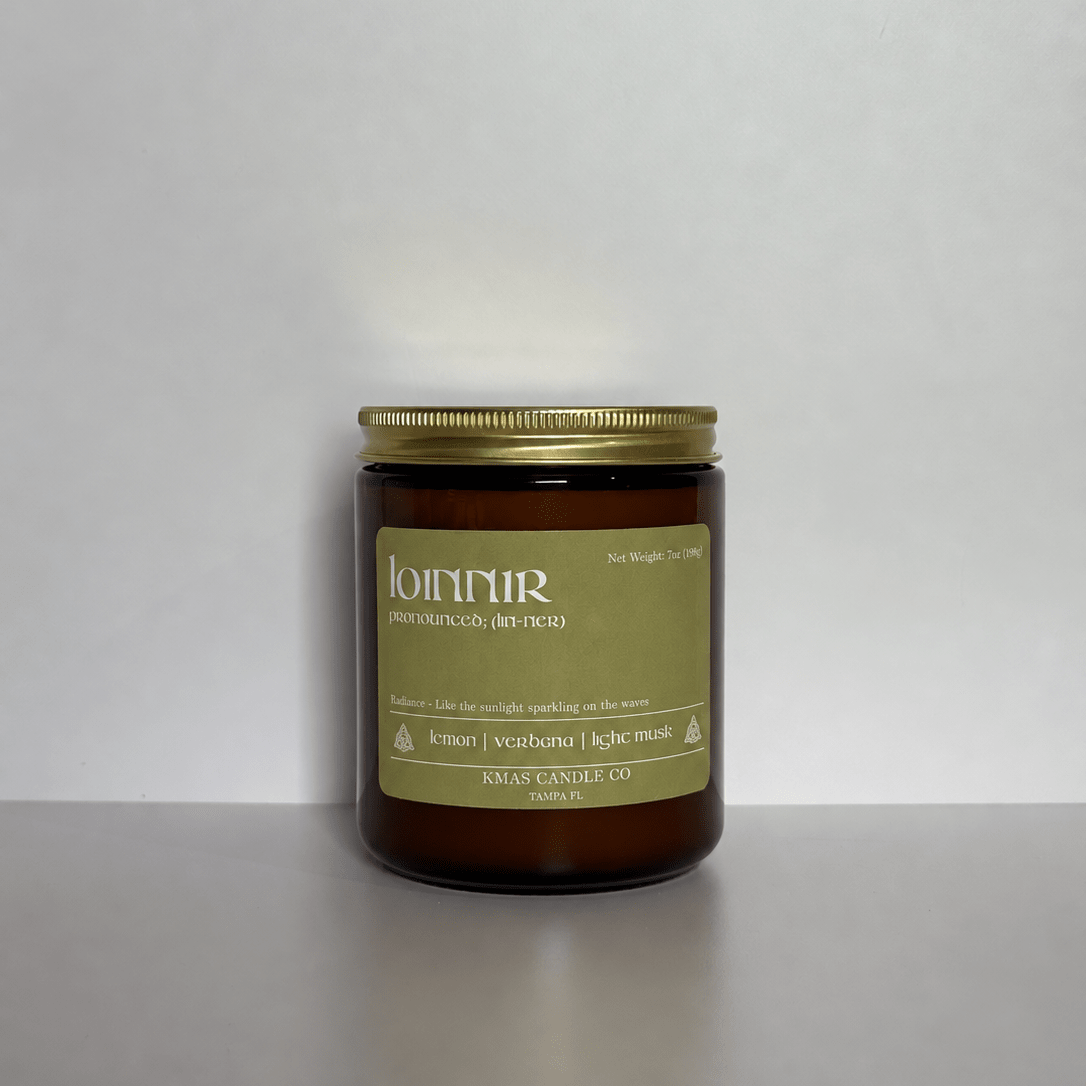 Loinnir | Wooden Wick Candle - KMAS Candle Co-Candles-KMAS Candle Co-A single amber glass jar candle with a gold metal lid and a muted olive-green label, set against a plain light gray background.