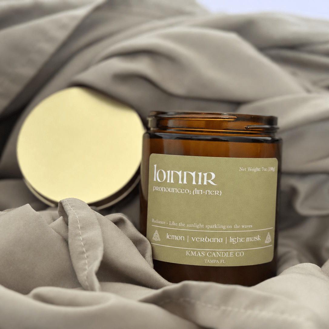 Loinnir | Wooden Wick Candle - KMAS Candle Co-Candles-KMAS Candle Co-An amber glass candle jar with a beige label reading 'lunnir' and 'Klagenfjord', placed on draped taupe fabric with its gold-toned lid beside it.